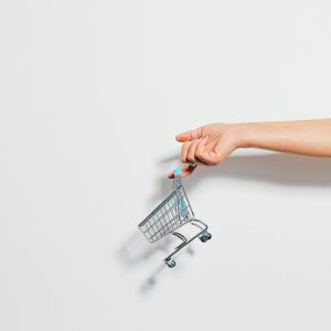 A hand holding a miniature shopping cart against a clean white background, emphasizing simplicity.